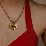Gold necklace with a bow pendant worn by a person in a red dress against a neutral background