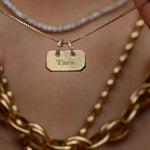 Close-up of layered gold necklaces with a name tag on a blurred background