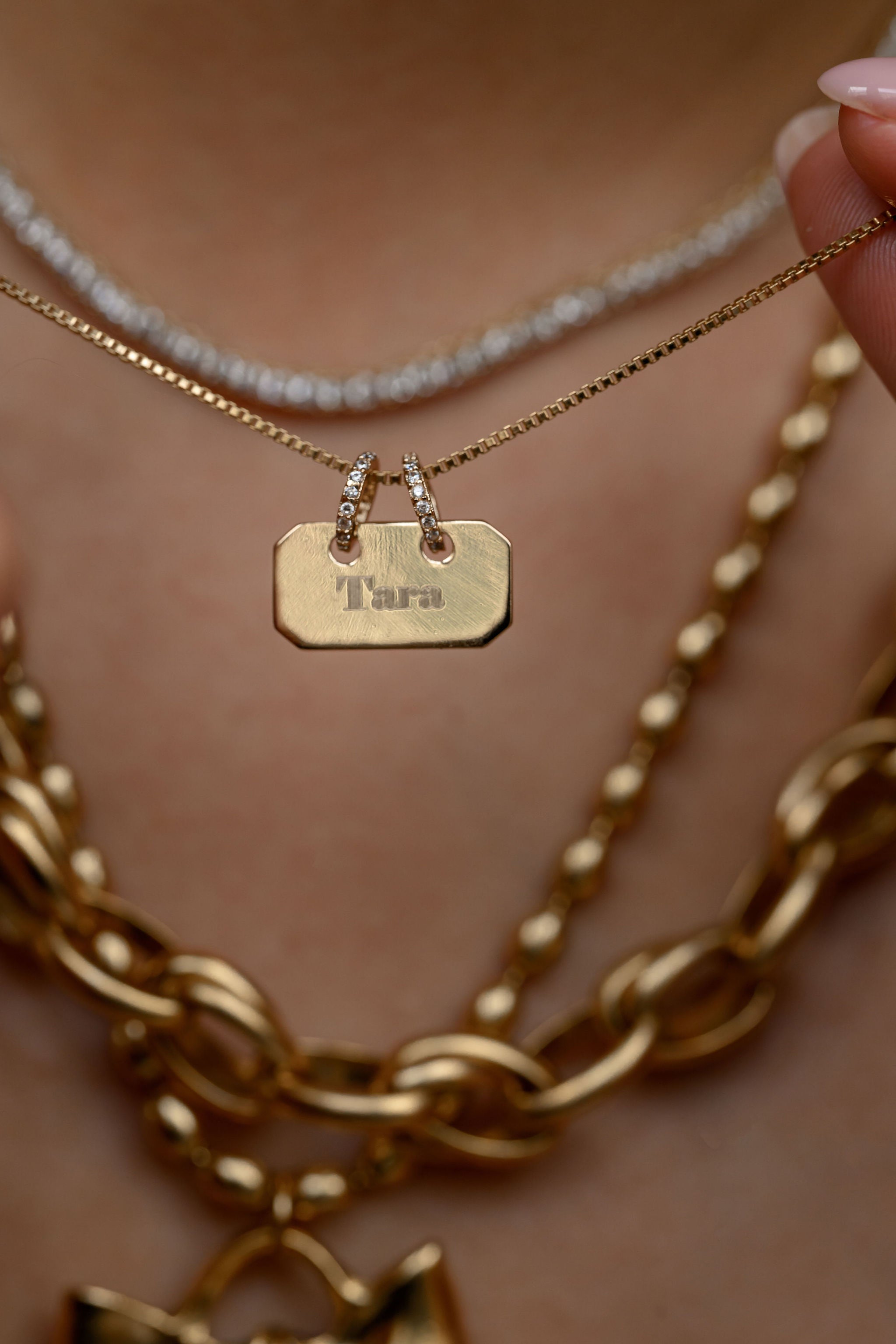 Close-up of layered gold necklaces with a name tag on a blurred background