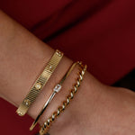 Gold bracelets on a wrist with a red background