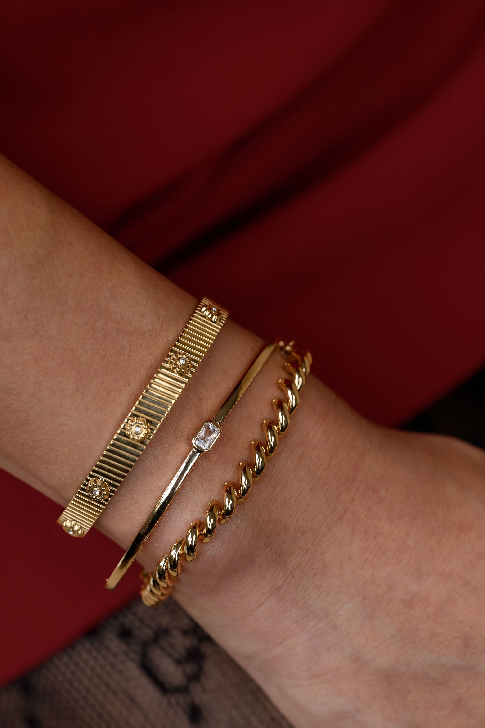 Gold bracelets on a wrist with a red background