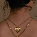 Gold necklace with heart and bow pendants on a person's neck.