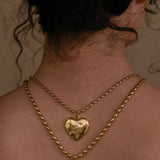 Gold necklace with heart and bow pendants on a person's neck.