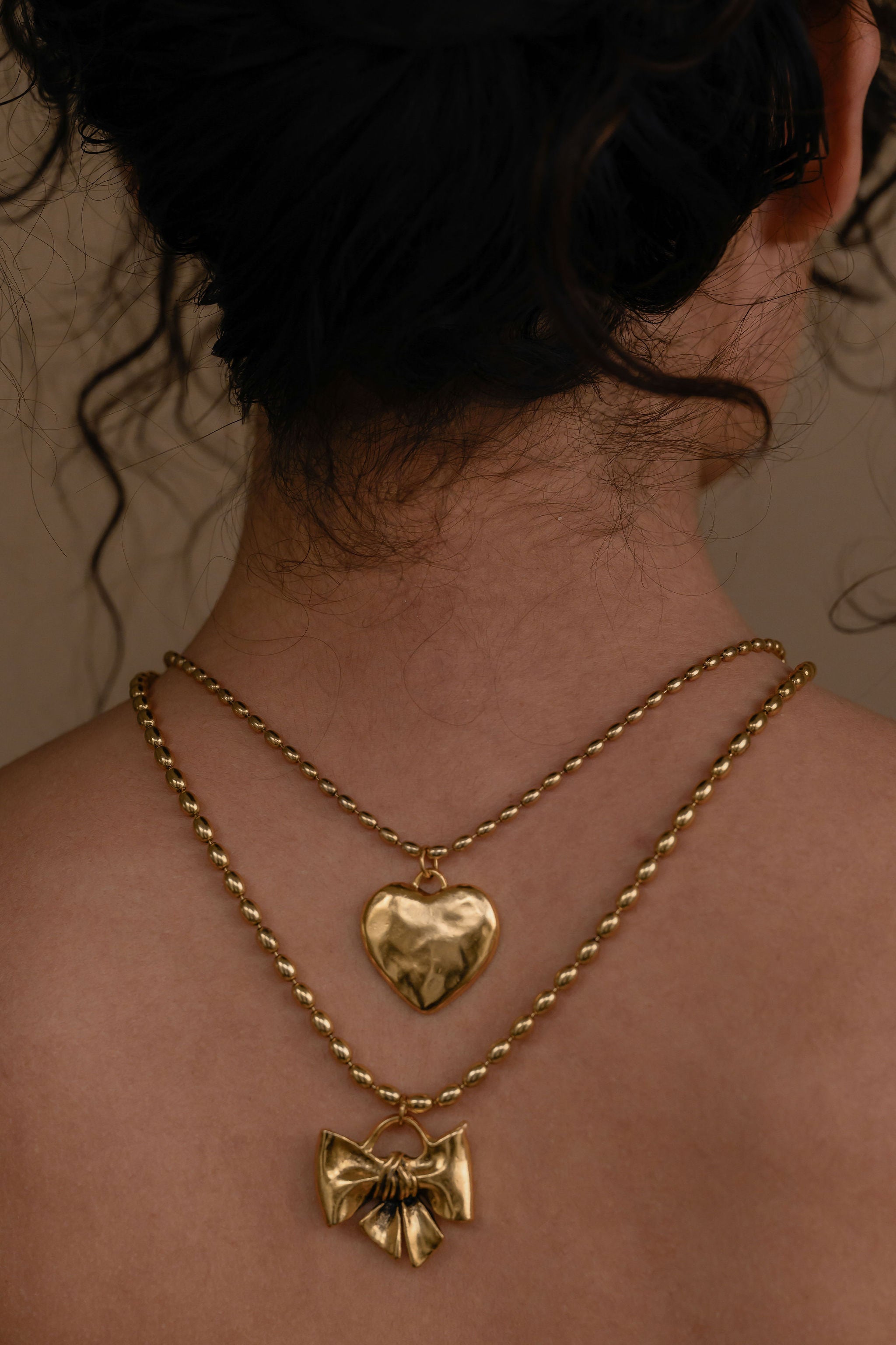 Gold necklace with heart and bow pendants on a person's neck.