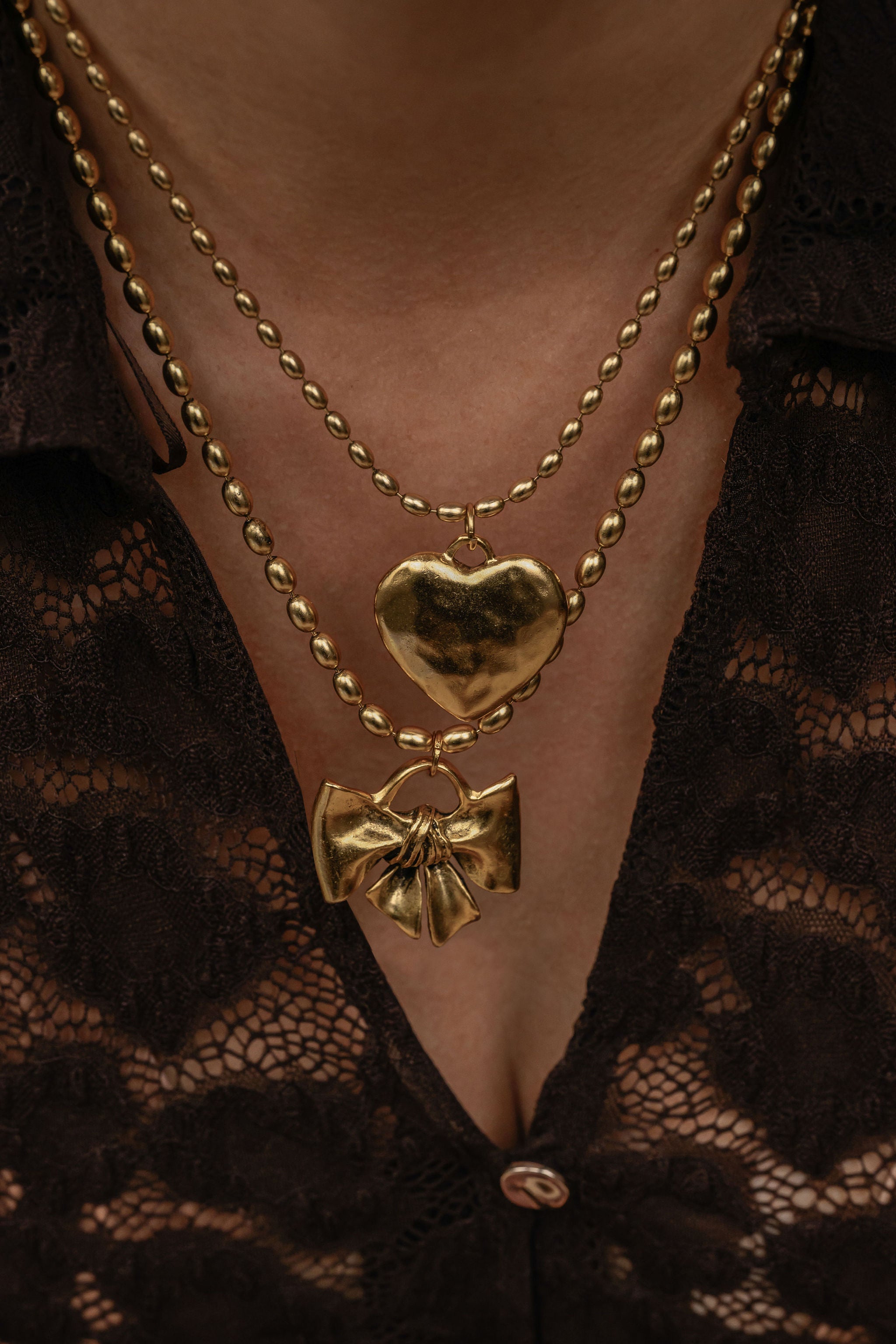 Gold necklace with heart and bow pendants on a lace garment.