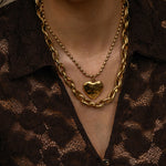 Close-up of a person wearing a gold chain necklace with a heart pendant on a brown textured background.