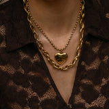 Close-up of a person wearing a gold chain necklace with a heart pendant on a brown textured background.
