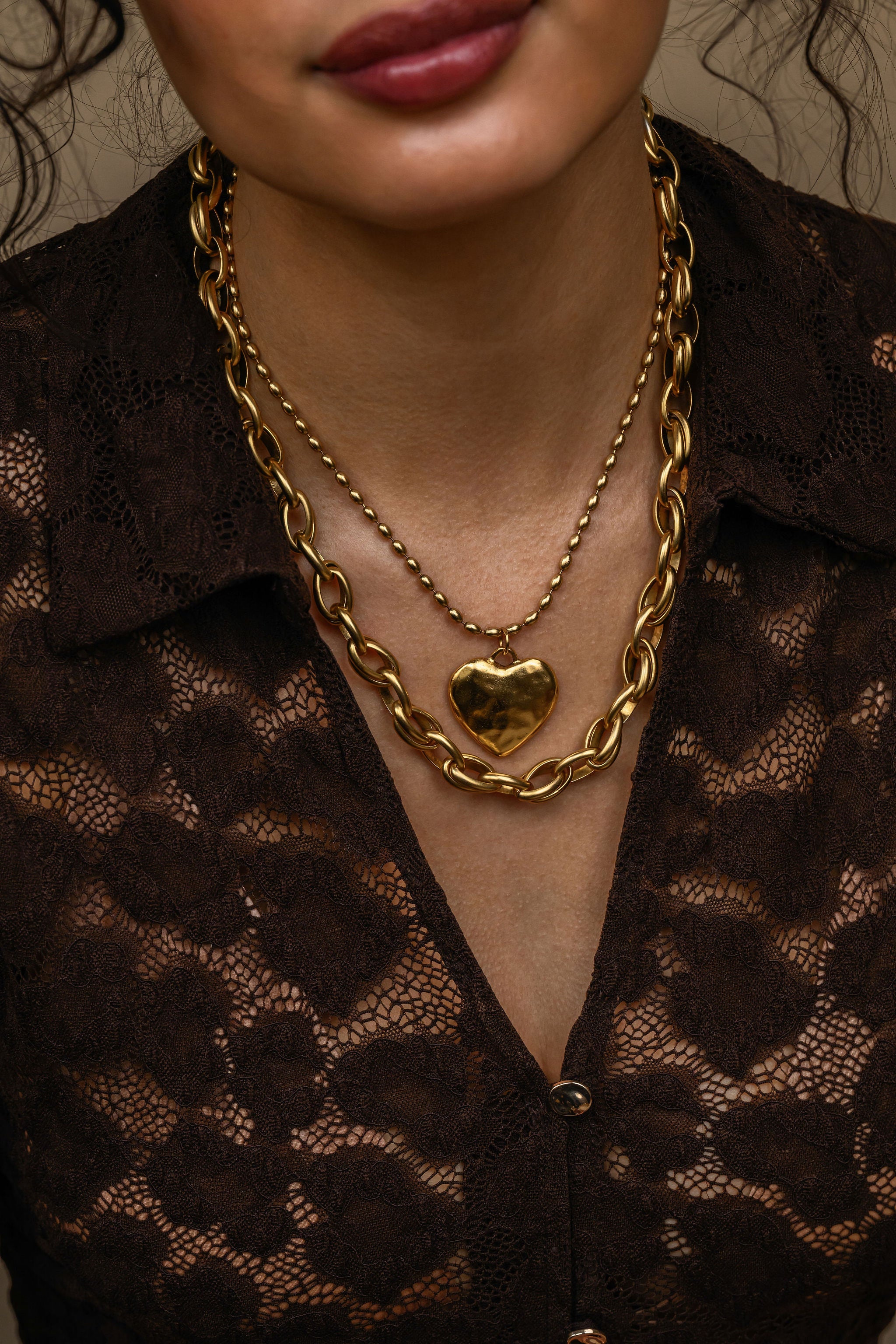 Close-up of a person wearing a gold chain necklace with a heart pendant on a brown textured background.