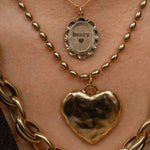 Gold necklaces with heart pendant and 'Henry' pendant on a person's neck.