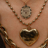 Gold necklaces with heart pendant and 'Henry' pendant on a person's neck.