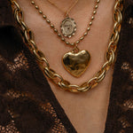 Close-up of a person wearing gold necklaces with a heart pendant on a lace garment.