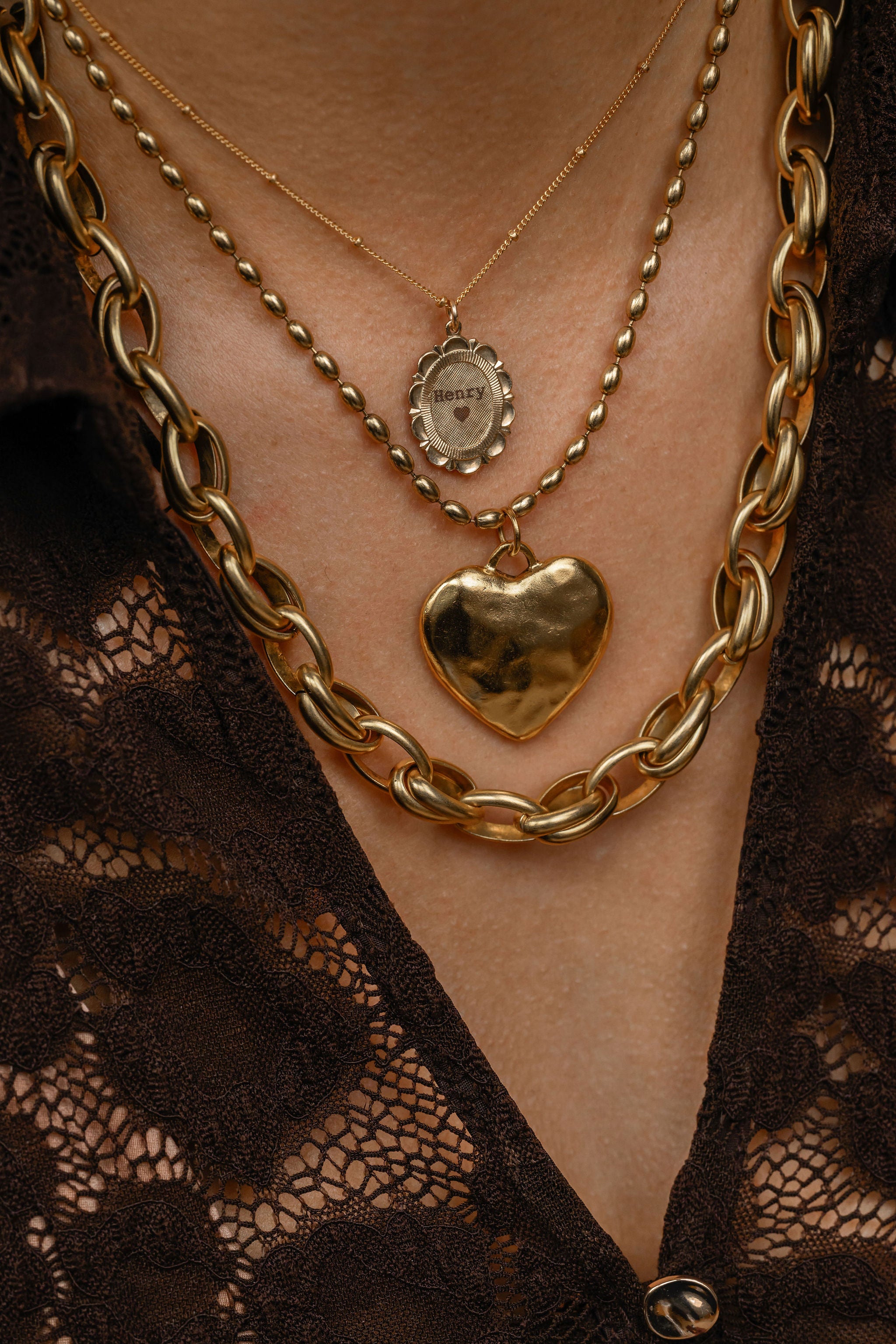 Close-up of a person wearing gold necklaces with a heart pendant on a lace garment.