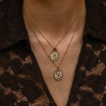 Close-up of a person wearing two necklaces with intricate designs against a dark lace garment.