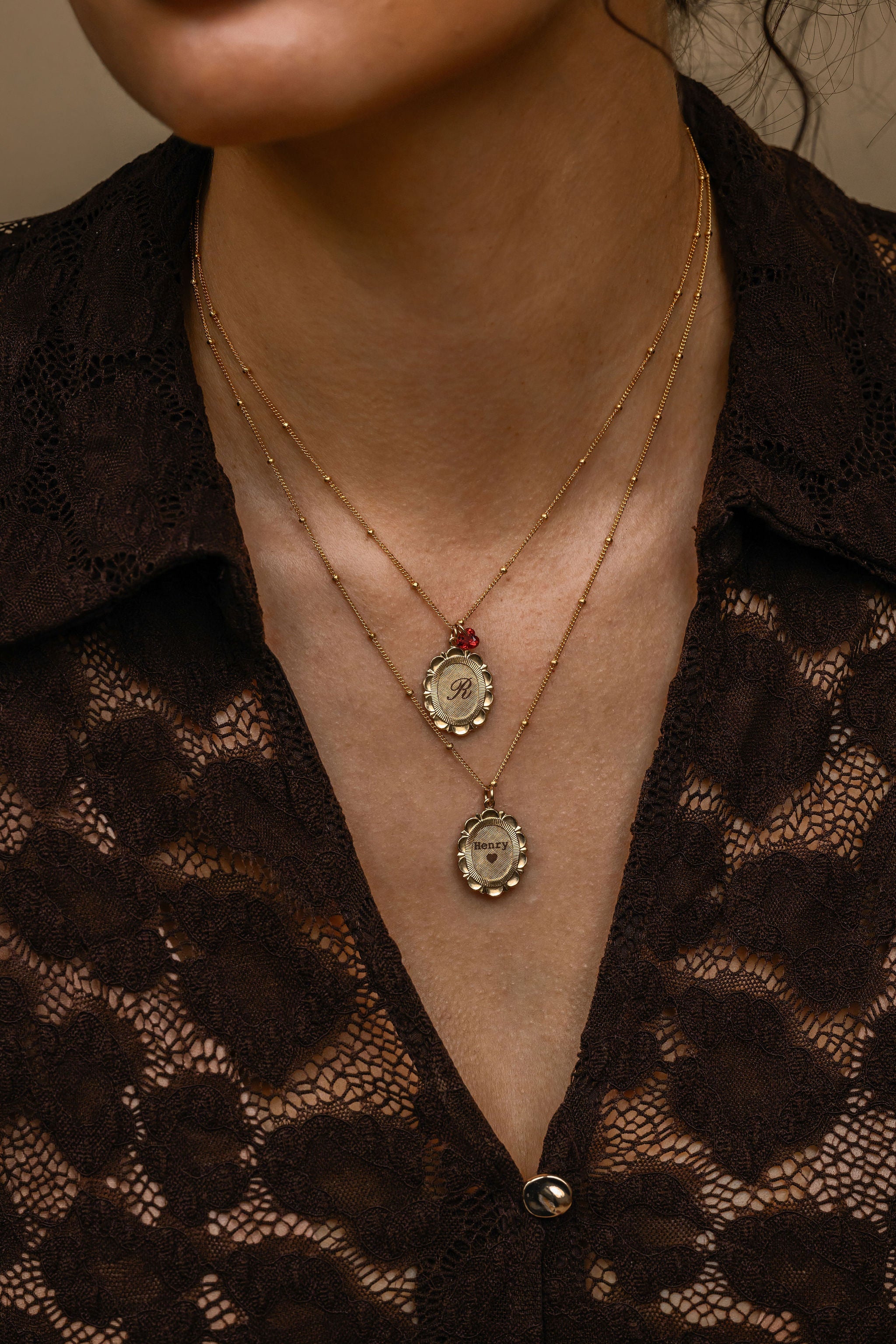 Close-up of a person wearing two necklaces with intricate designs against a dark lace garment.