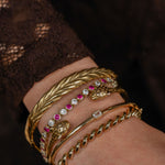 Close-up of a wrist wearing gold bracelets with gemstones on a dark background