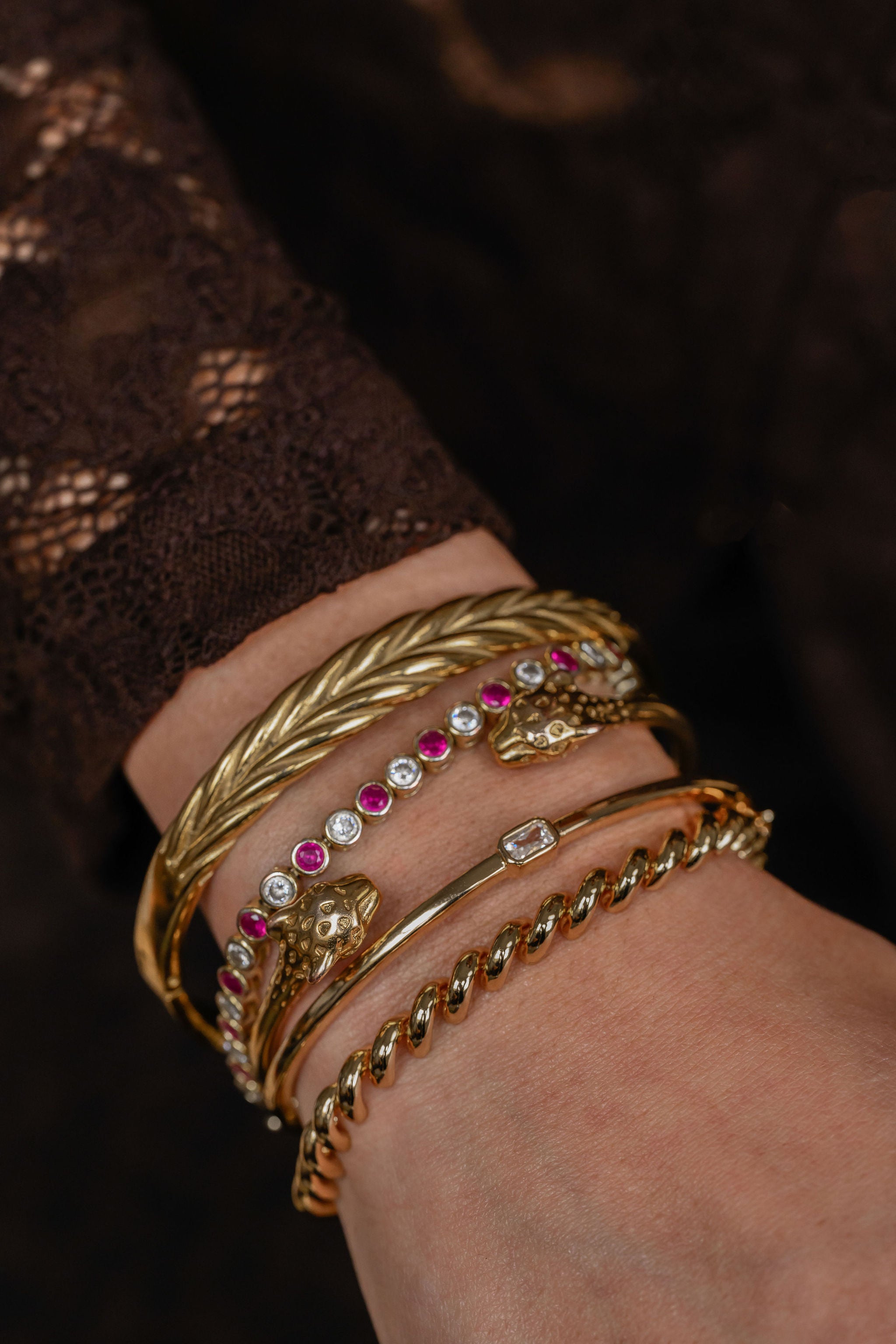 Close-up of a wrist wearing gold bracelets with gemstones on a dark background