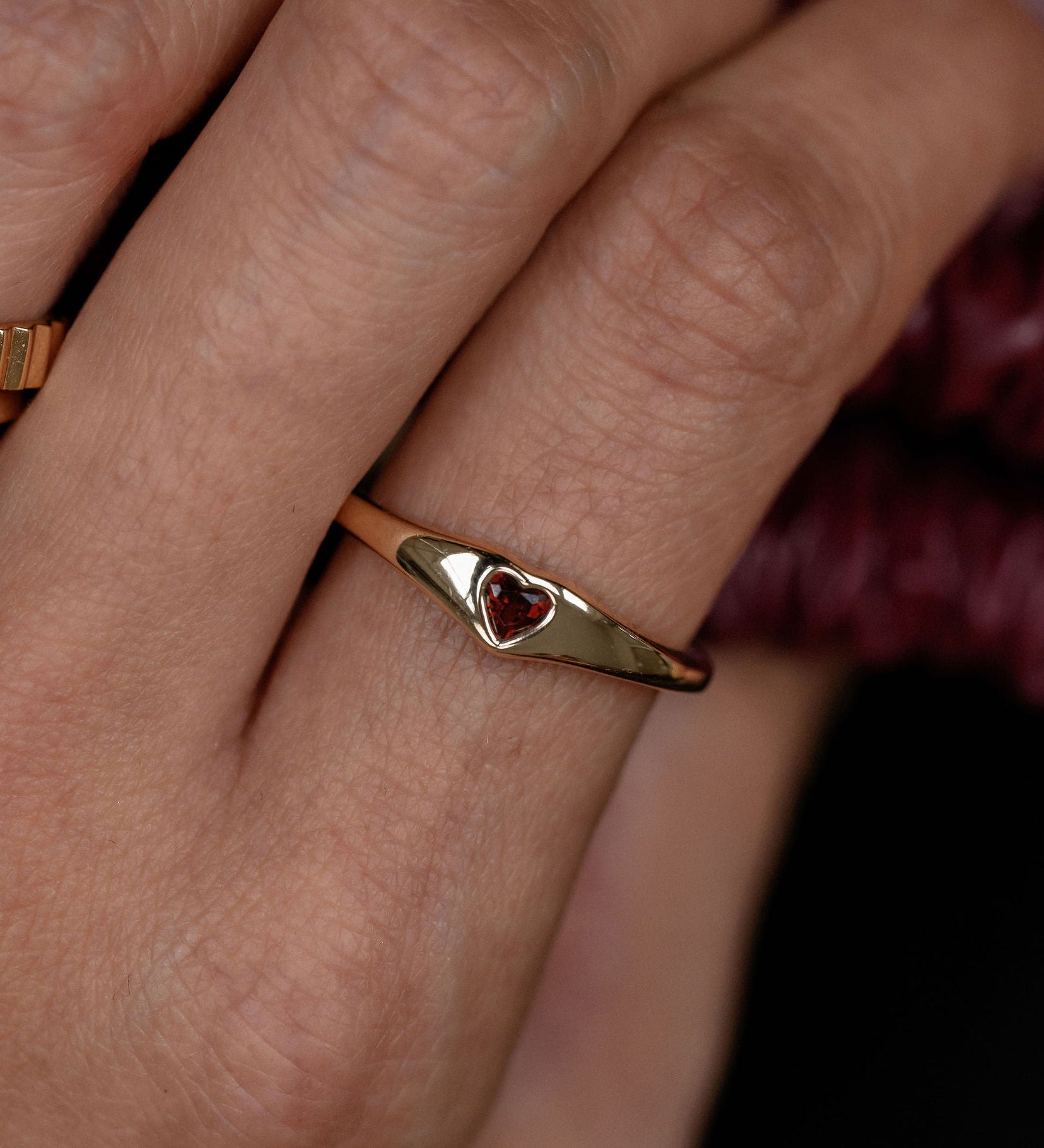Close-up of a hand wearing a gold ring with a red gemstone on a dark background