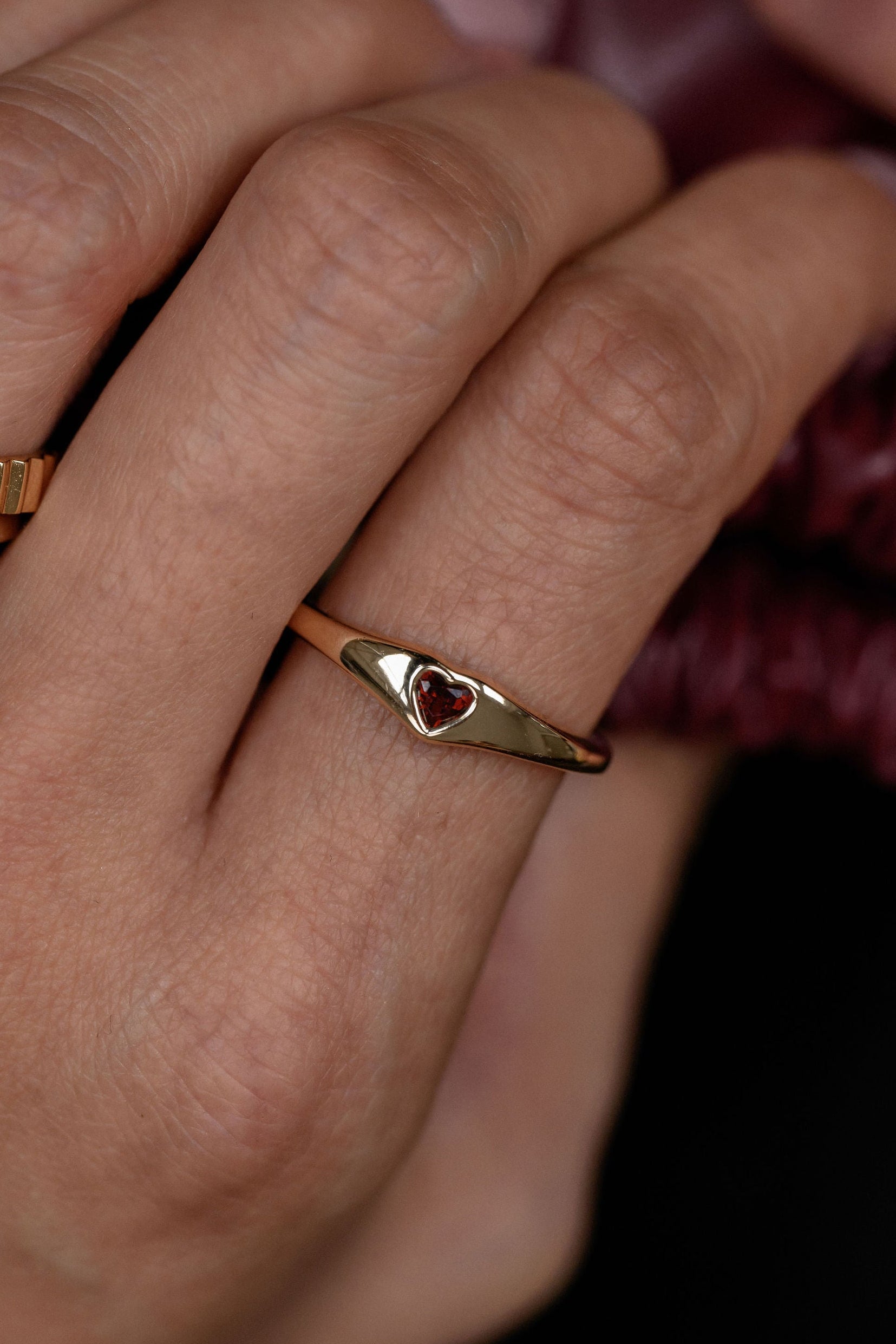 Close-up of a hand wearing a gold ring with a red gemstone on a dark background