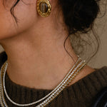 Close-up of a person wearing gold earrings and layered necklaces.
