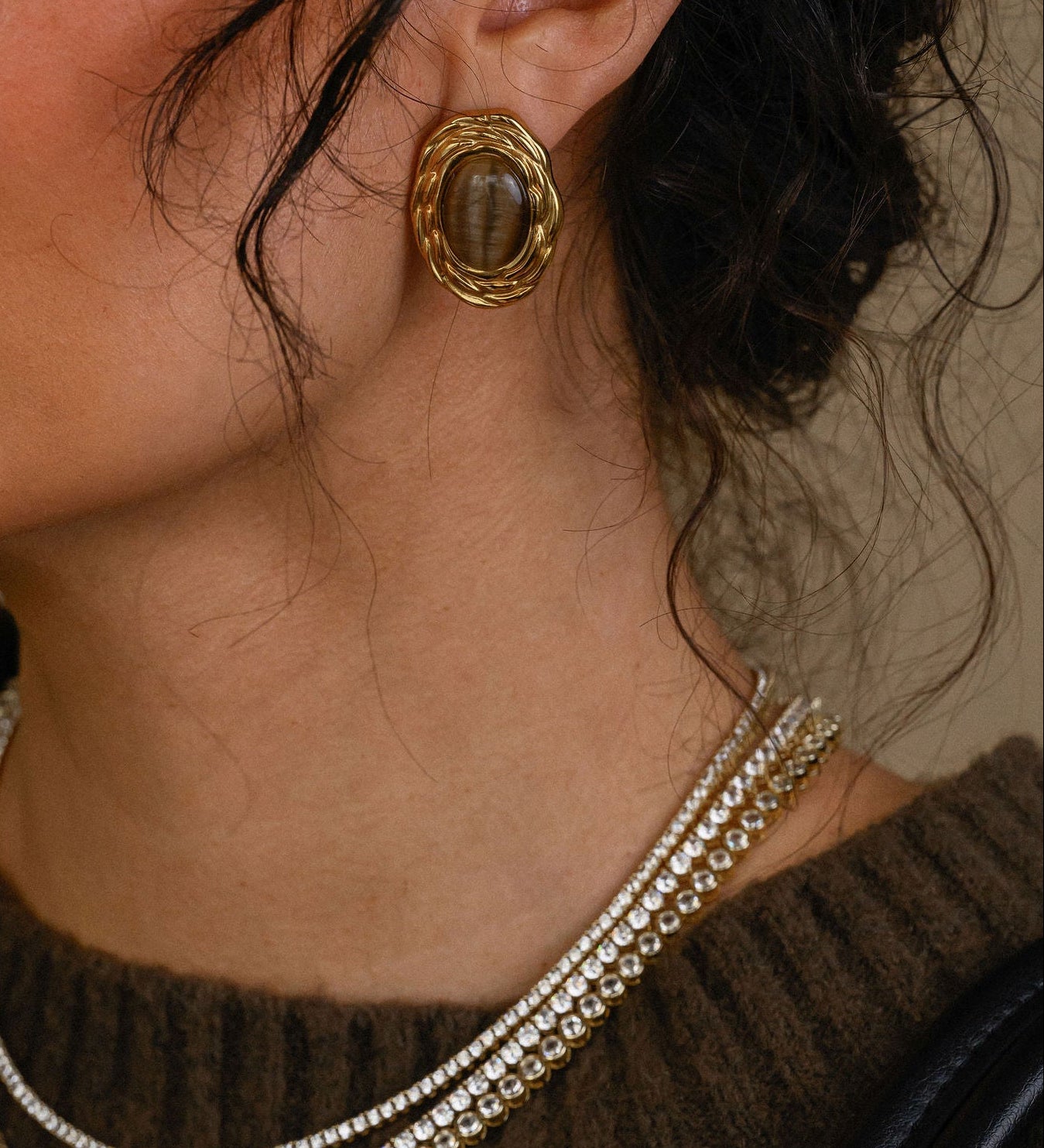 Close-up of a woman wearing gold earrings and a necklace, holding a black handbag.