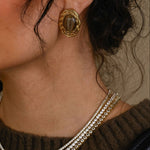 Close-up of a woman wearing gold earrings and a necklace, holding a black handbag.