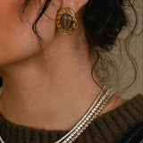 Close-up of a woman wearing gold earrings and a necklace, holding a black handbag.