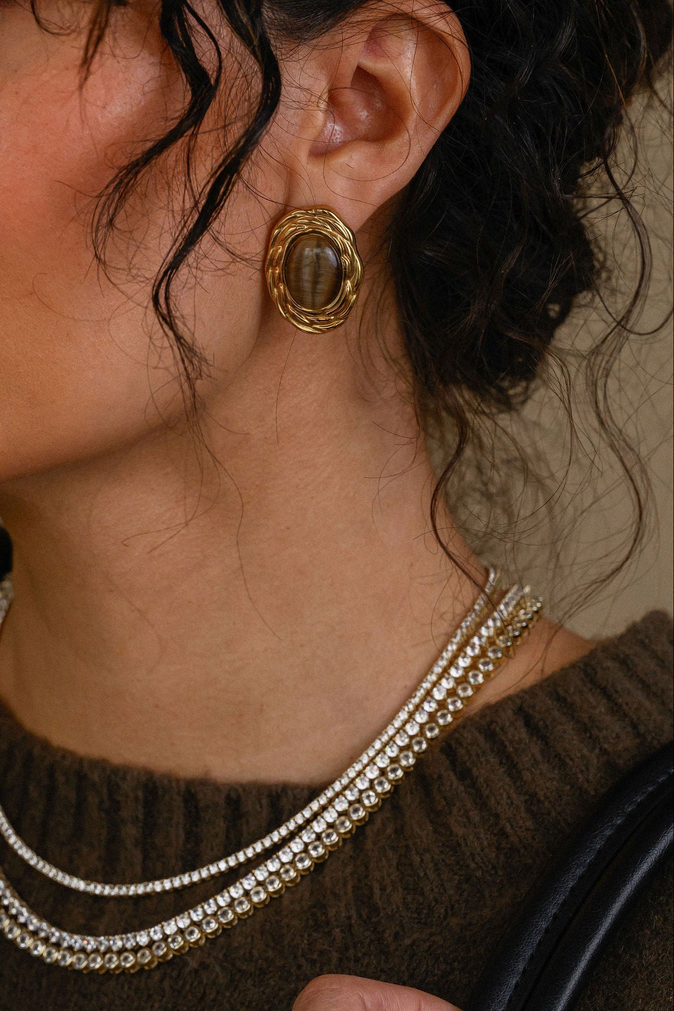 Close-up of a woman wearing gold earrings and a necklace, holding a black handbag.