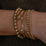 Gold bracelets on a wrist against a dark background