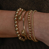 Gold bracelets on a wrist against a dark background
