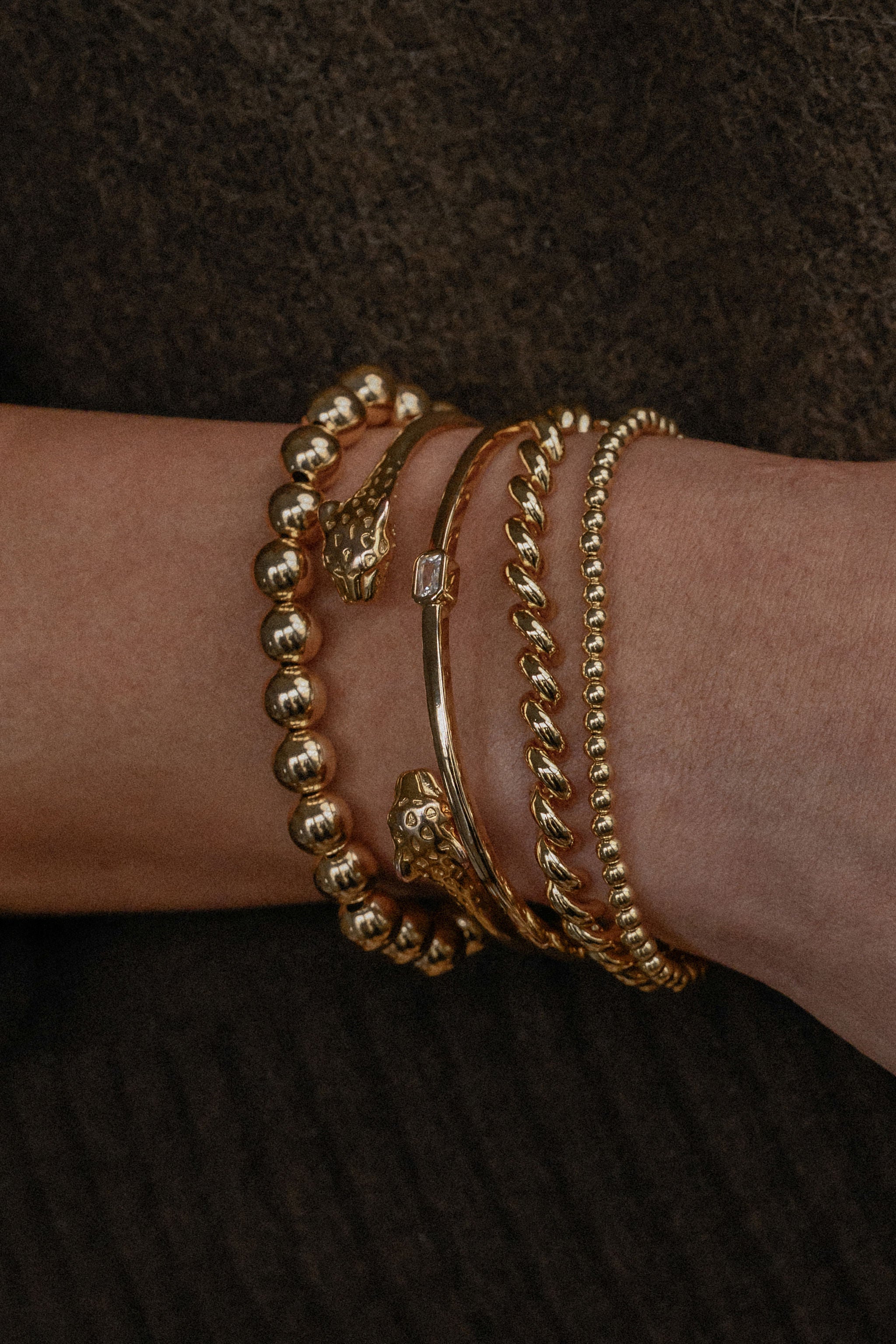 Gold bracelets on a wrist against a dark background