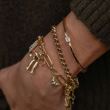 Gold anklets with charms on a wrist against a dark background