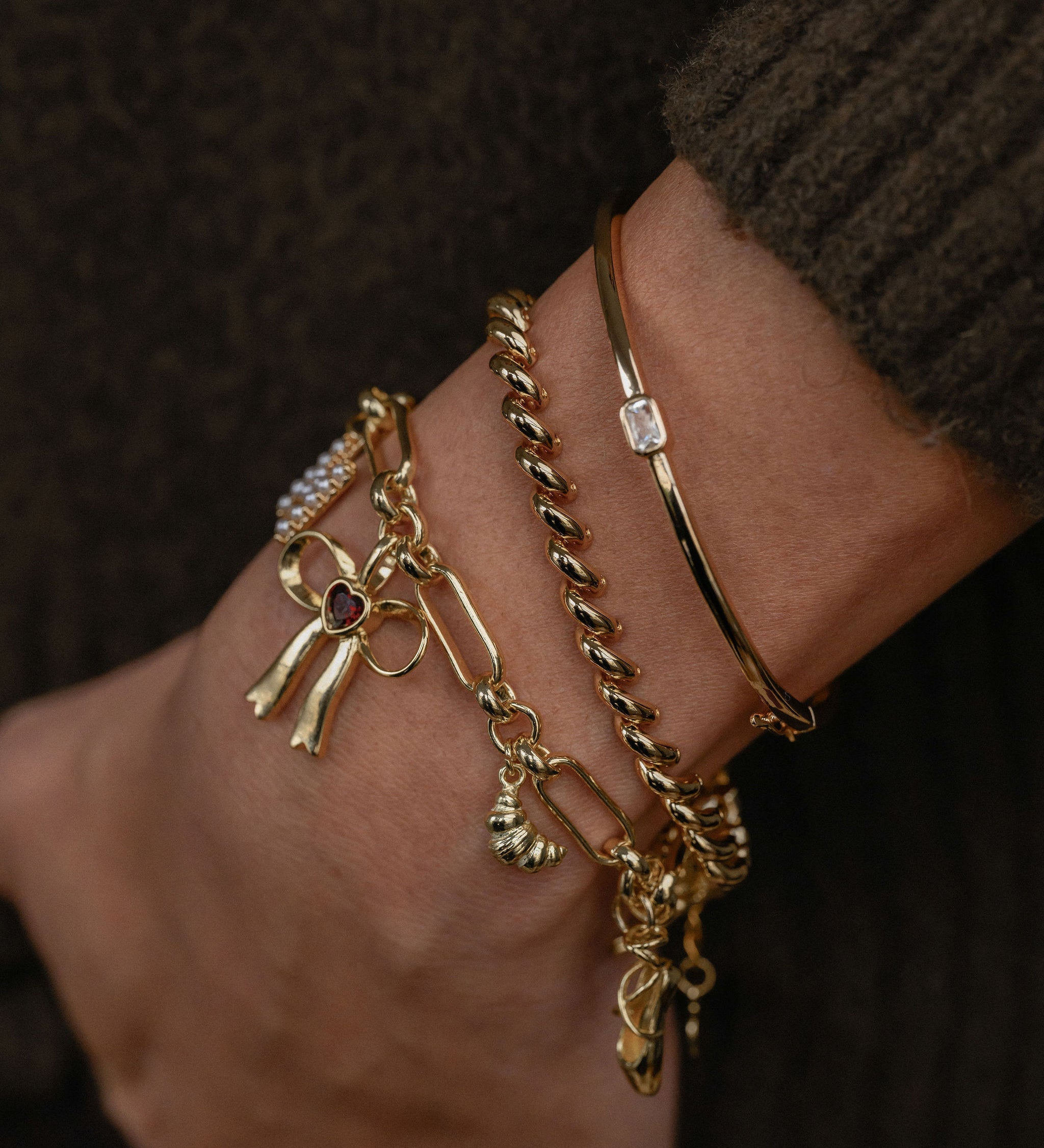 Gold anklets with charms on a wrist against a dark background
