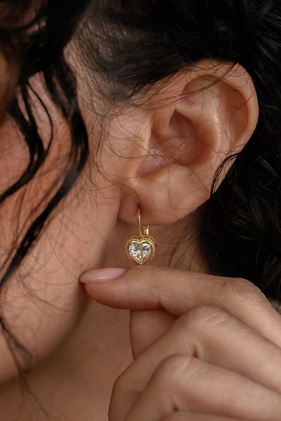 Close-up of a woman wearing a gold earring with a heart design.