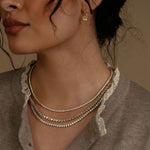 Close-up of a woman wearing layered necklaces and an earring against a neutral background
