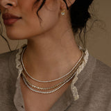 Close-up of a woman wearing layered necklaces and an earring against a neutral background