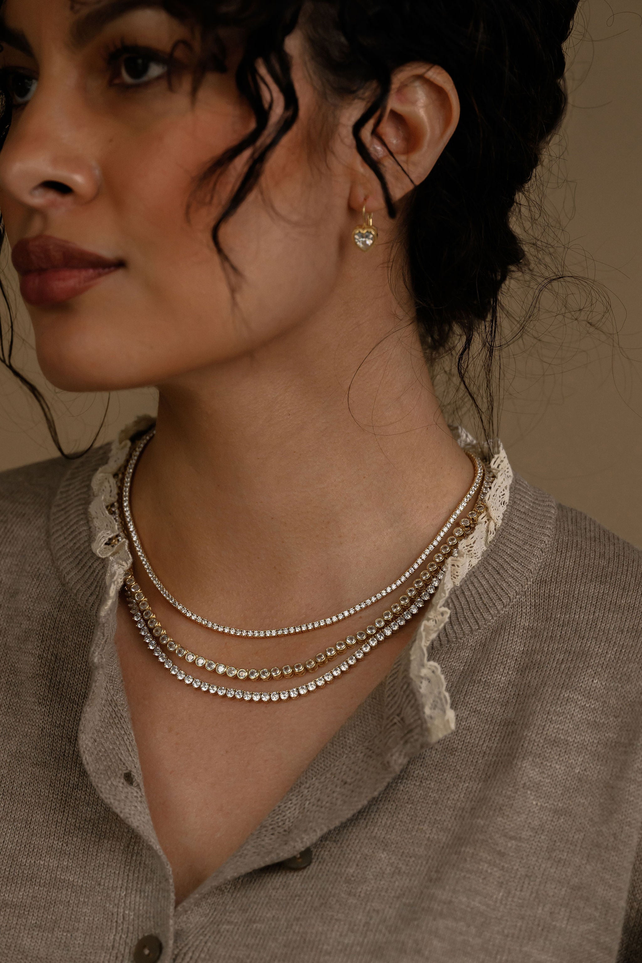 Close-up of a woman wearing layered necklaces and an earring against a neutral background