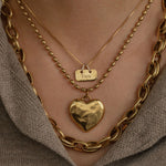 Gold chain necklace with a heart pendant worn by a person against a neutral background