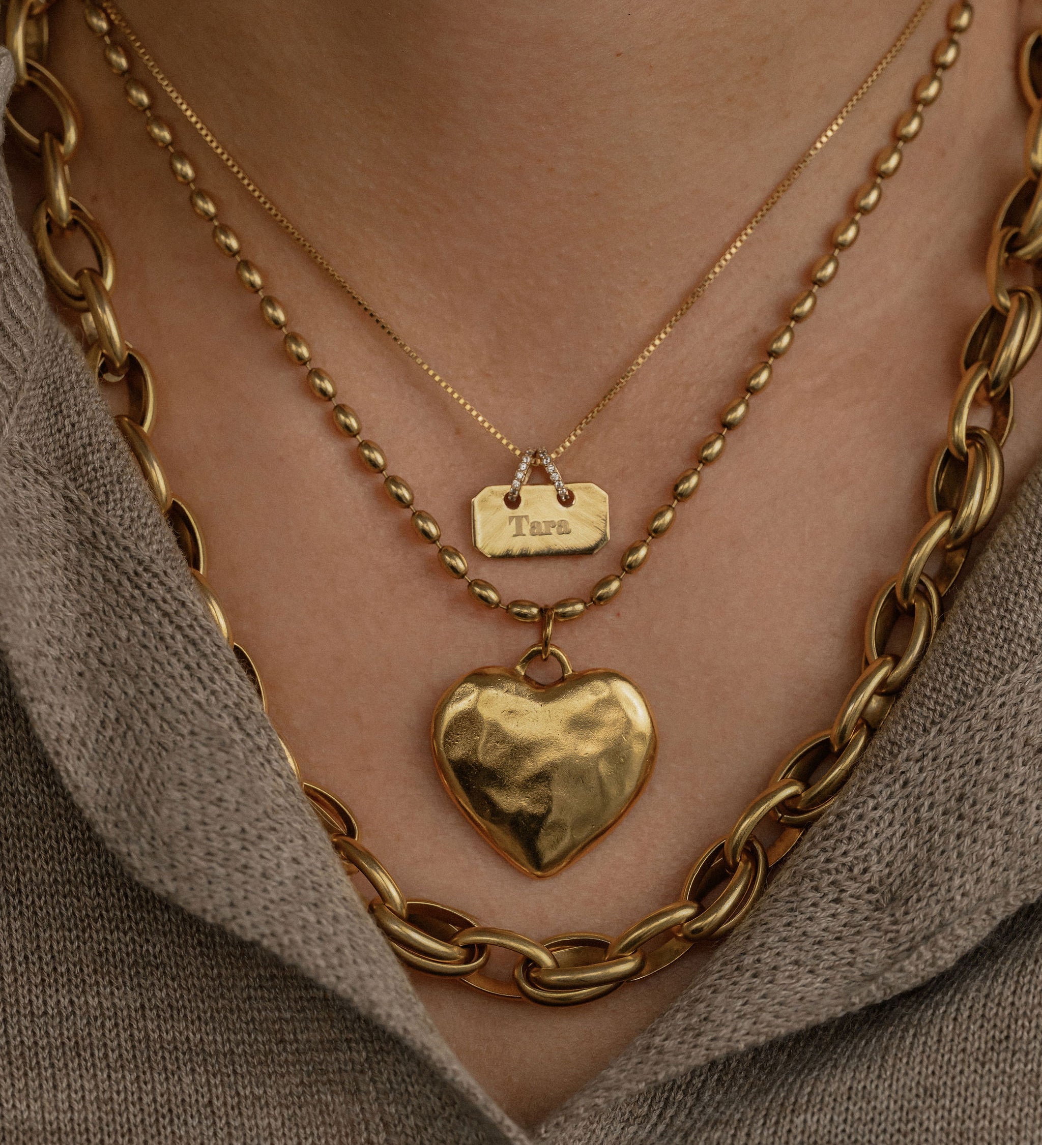 Gold chain necklace with a heart pendant worn by a person against a neutral background