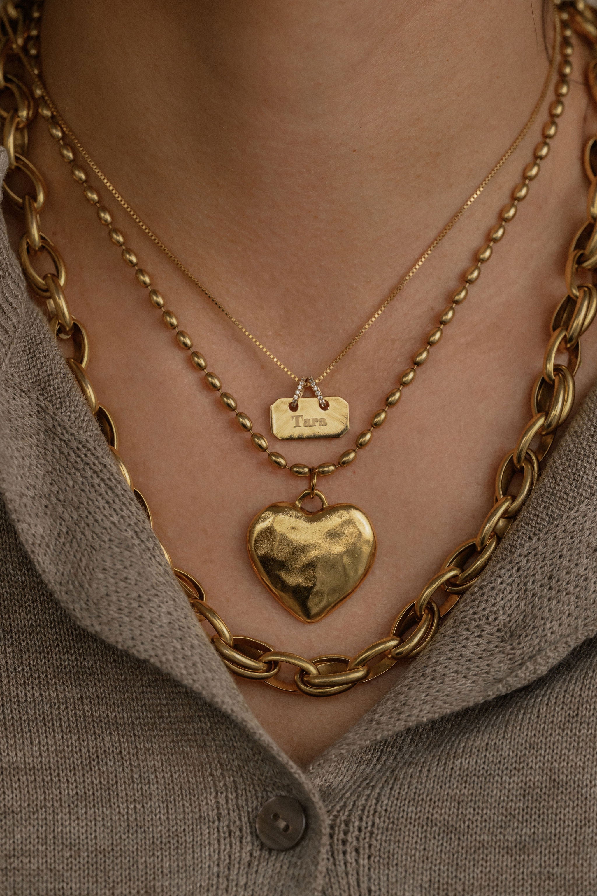Gold chain necklace with a heart pendant worn by a person against a neutral background