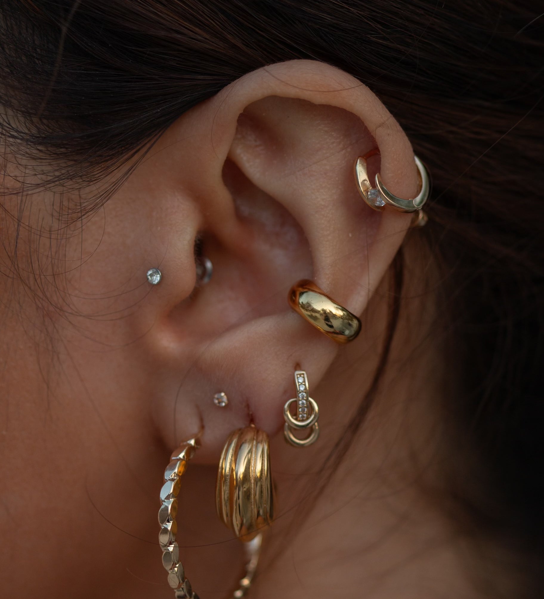 Close-up of an ear with multiple gold and crystal earrings 