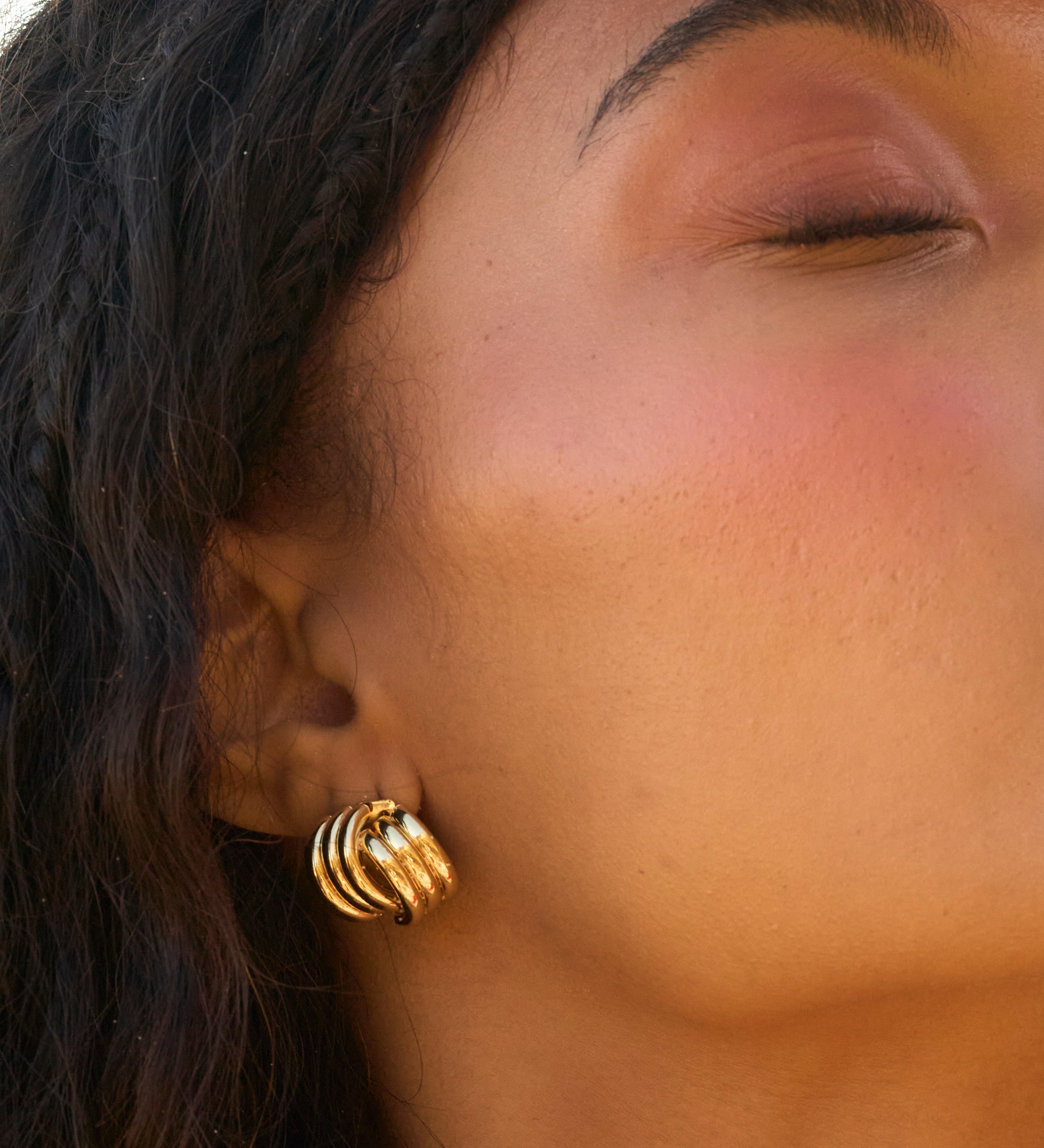 A woman with her eyes closed wearing gold earrings