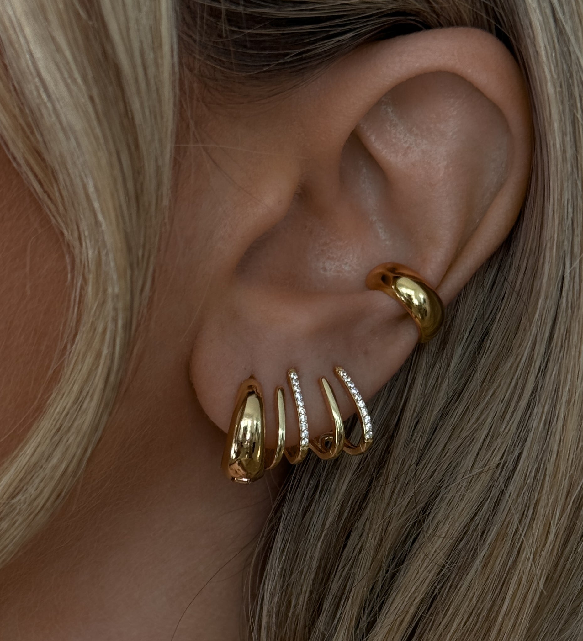 Close-up of an ear with multiple gold and crystal earrings 