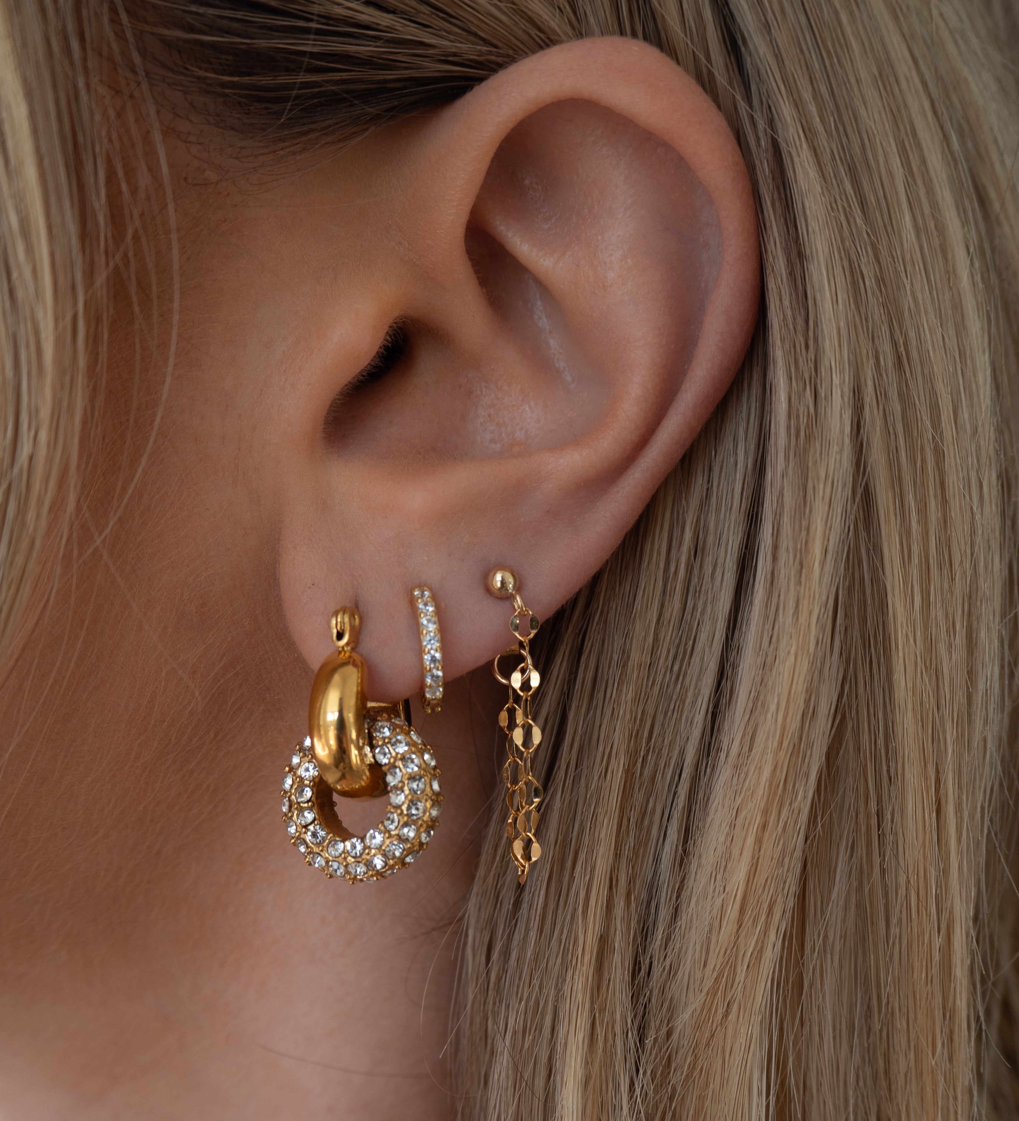 Close-up of an ear with multiple gold and crystal earrings 
