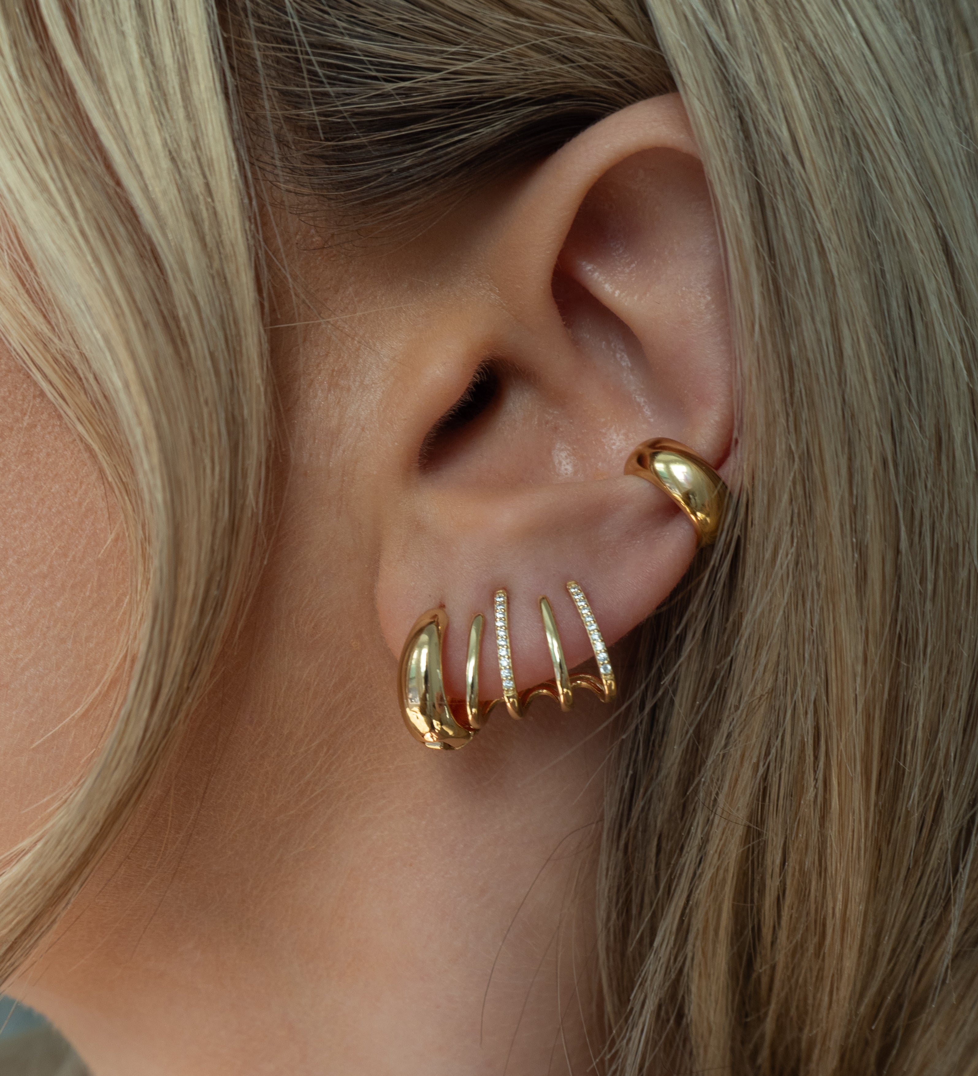 Close-up of an ear with multiple gold and crystal hoop earrings 