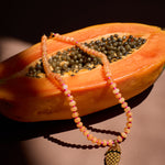Necklace with a fish pendant draped over a halved papaya on a dark background