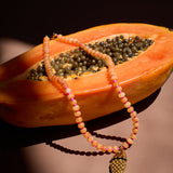 Necklace with a fish pendant draped over a halved papaya on a dark background