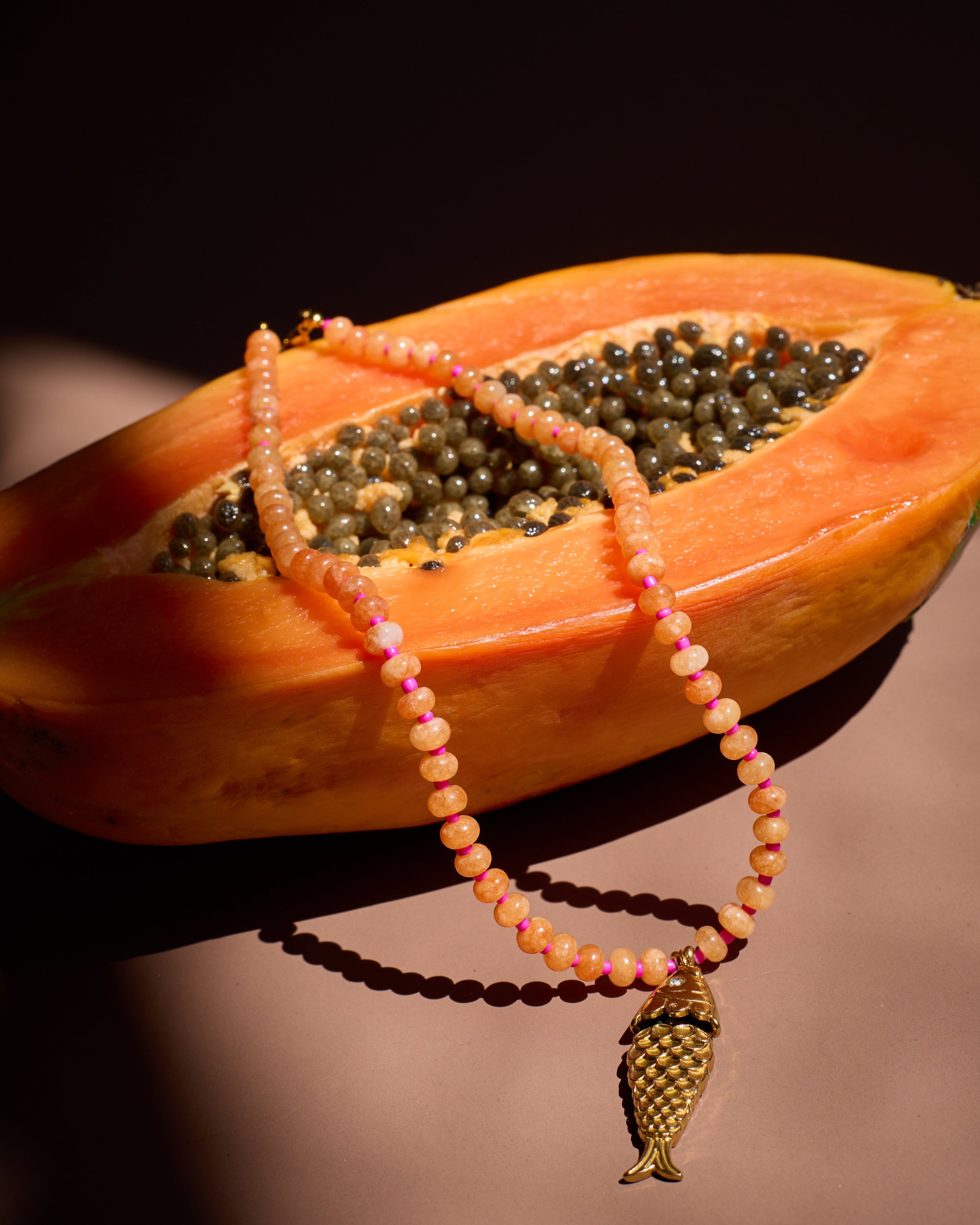Necklace with a fish pendant draped over a halved papaya on a dark background