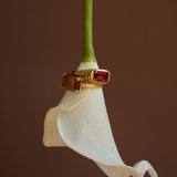 Gold ring with a red gemstone on a white flower against a brown background