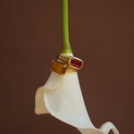 Gold ring with a red gemstone on a white flower against a brown background