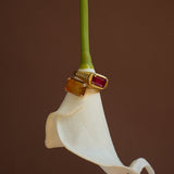 Gold ring with a red gemstone on a white flower against a brown background